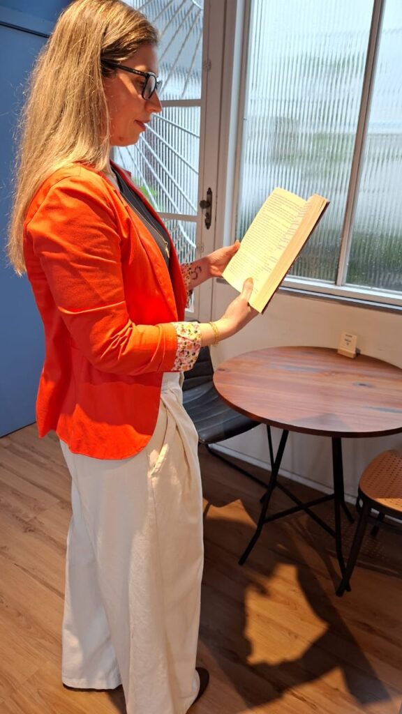 Dra. Camila Castellan lendo um livro em pé, perto da janela