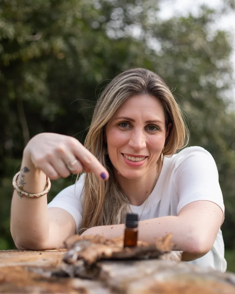 Dra. Camila Castellan sorrindo, com um frasco de óleo essencial sobre a mesa